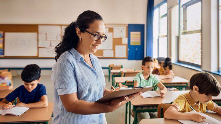 A school staff member observes students in a classroom while holding an observation checklist on a clipboard